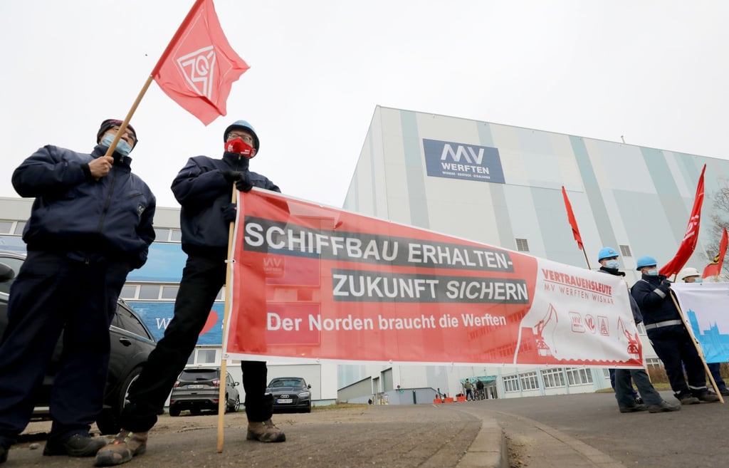 Beschäftigte der Werft stehen mit Fahnen und Transparenten vor der Schiffbauhalle in Wismar.