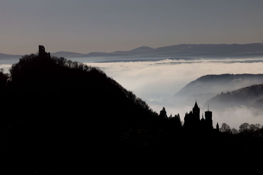 Hinter Schloss Drachenburg (r) und der Burg Drachenfels ziehen Nebelschwaden durch das Rheintal.