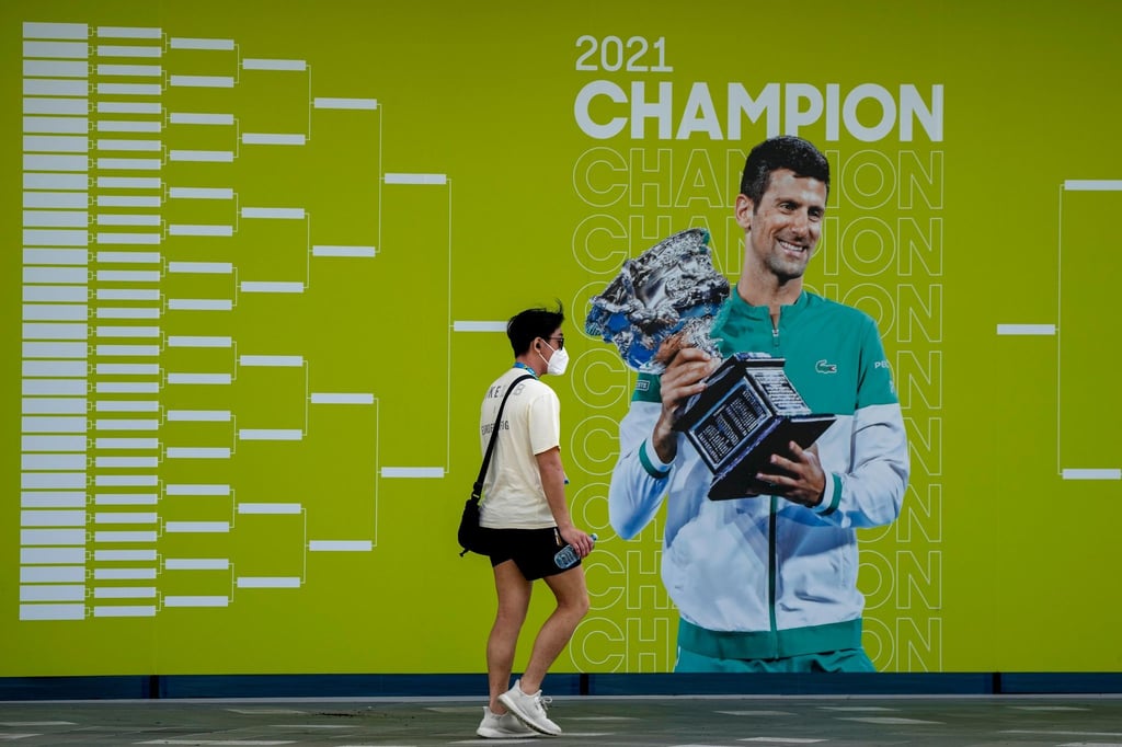 Ein Mann geht an einem Plakat mit dem serbischen Titelverteidiger Novak Djokovic im Melbourne Park vorbei.