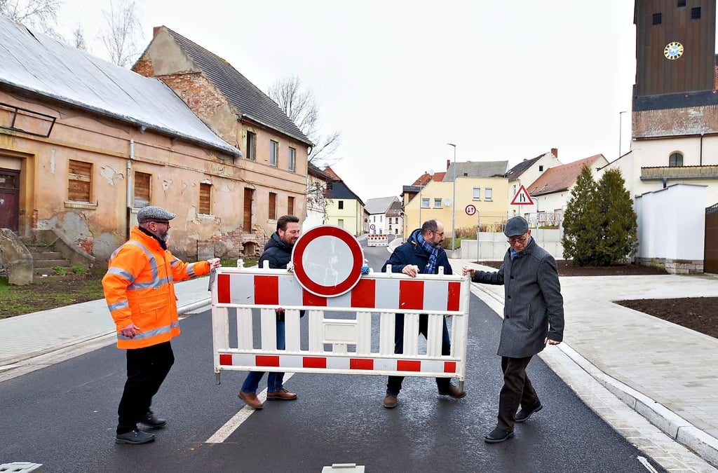Oliver Grafe von der Landesstraßenbaubehörde, Thomas Richter vom Baubetrieb HTS, Bürgermeister Thomas Schneider und Ortsbürgermeister Dirk Honsa (v. li.) räumen einen Absperrzaun von der Fahrbahn.
