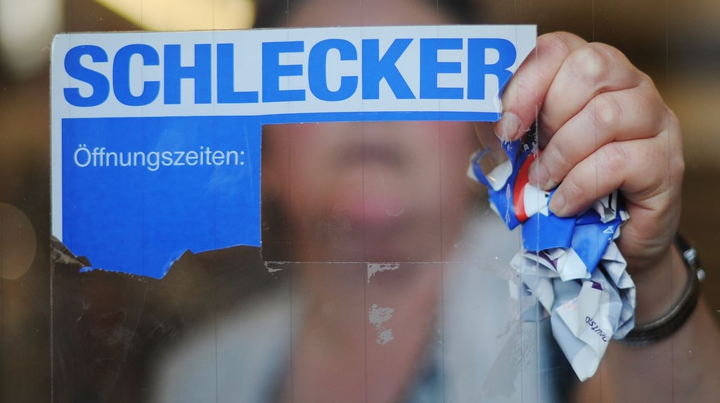 Eine Schlecker-Mitarbeiterin reißt das Firmenlogo von der Eingangstür einer Filiale.