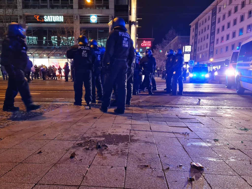 Scherben von auf Polizisten geworfenen Flaschen liegen neben den Beamten auf einem Bürgersteig in Magdeburg.