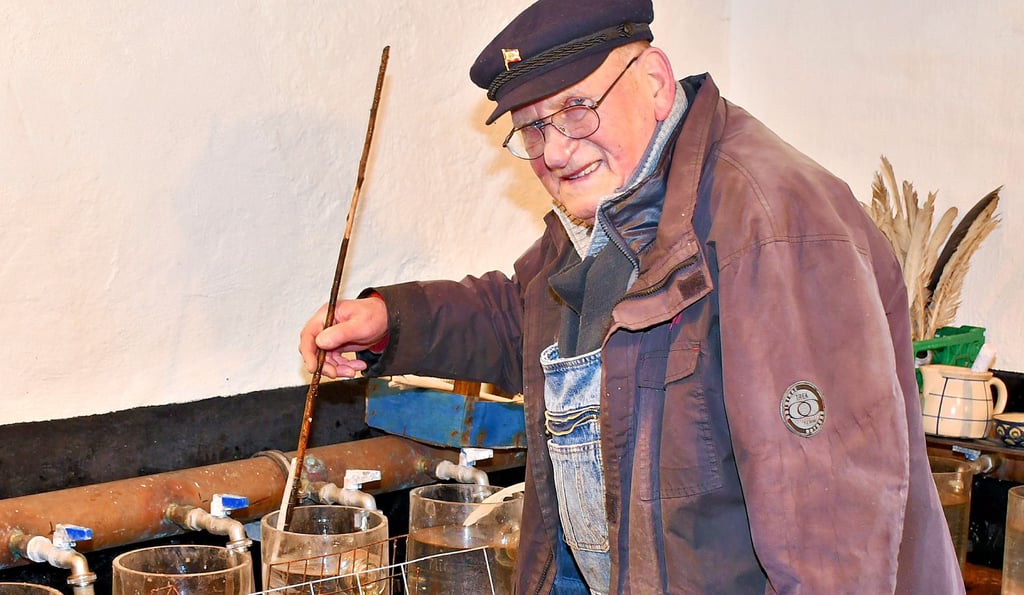 Fischer Wilfried Kagel rührt mit einer an einem Stock befestigten Schwanenfeder vorsichtig in den Zugergläsern.