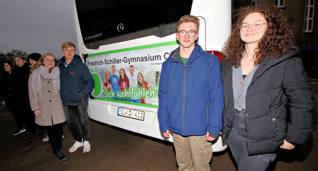 Antonia, Jonas, Julia und Moritz stehen hier neben dem Werbeaufdruck für das Schillergymnasium am Bus, der die Schüler täglich zur Schule und wieder nach Hause bringt.