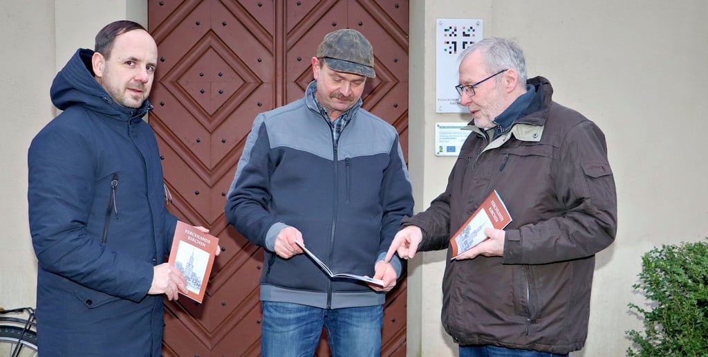 Buchautor Horst Wedau zeigt Ronald Mund vom Gemeindekirchenrat und Daniel Richter, Vorsitzender des Heimatvereins Ferchland (v. re.), vor dem Eingang zur Kirche sein neuestes Werk.