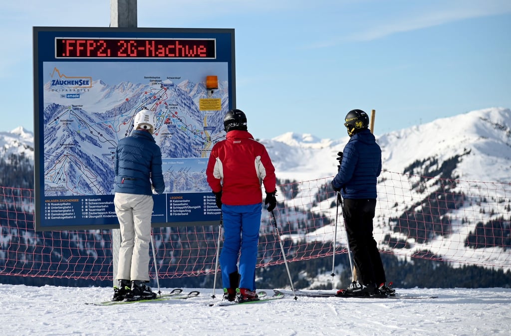 Skifahrer vor einer Informationstafel mit der Aufforderung nach FFP2-Masken und 2G-Nachweis im Skigebiet Altenmarkt-Zauchensee.