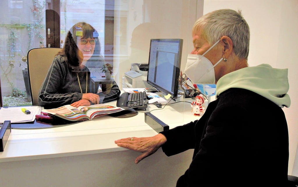 Kerstin Jacob berät eine Kundin im Reisebüro von Schubert Touristik in der Taubenstraße. Scheibe und Maske schützen auf beiden Seiten.