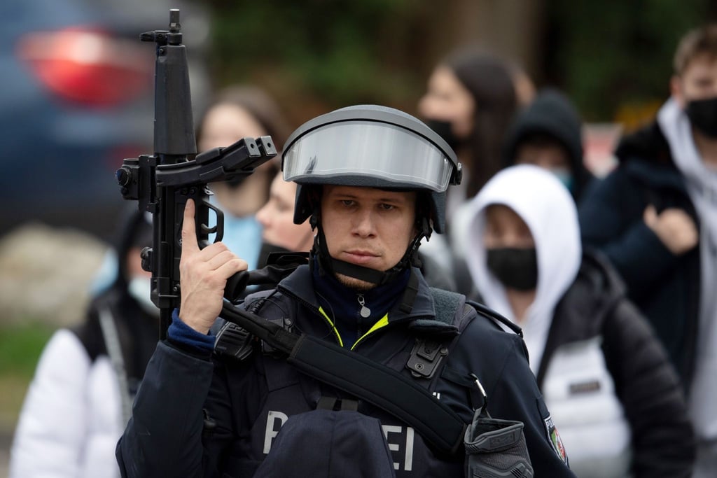 Ein schwerbewaffneter Polizist sichert Schüler, die aus der Schule geführt werden.