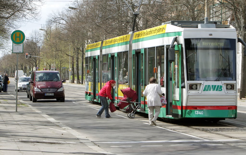 Eine Frau hievt einen Kinderwagen in die Straßenbahn am Westfriedhof in Magdeburg.