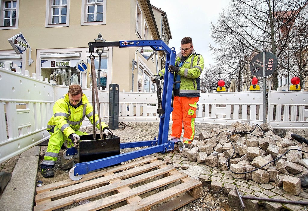 David Ehmig (l.) und René Schönfeld arbeiten an der Reparatur der Polleranlage an der Westseite des Zeitzer Roßmarktes. Sie setzen die Gehäuse ein, in die später die eigentlichen Poller gesetzt werden.