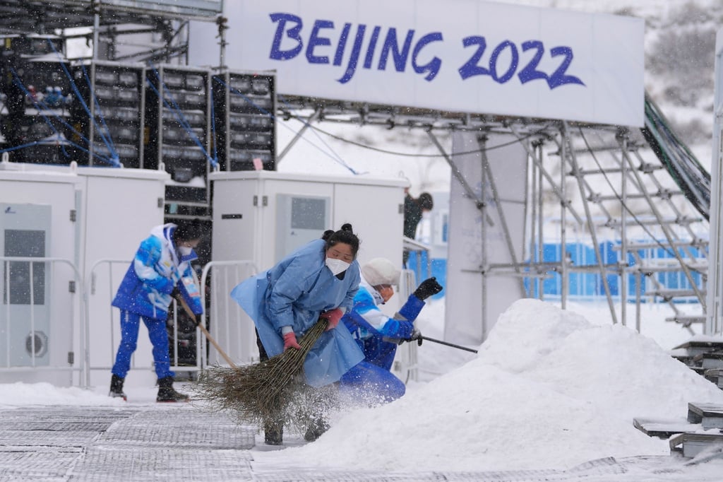 Im Nationalen Biathlonzentrum fegen Olympia-Mitarbeiter Schnee: Der Start der Männer-Biathlon-Staffel wird wegen Kälte verlegt.