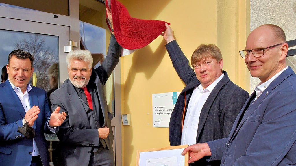 Energie- und Klimaschutzminister Armin Willingmann (2.v.l.) lüftete zusammen mit Verbandsgemeindebürgermeister Norbert Born das Schild am Verwaltungsamt Helbra, das die Kommune für ihr Energiemanagement auszeichnet. Auch Landrat André Schröder (l.) und Klimaschutzmanager Harald Henke (r.) freuen sich.