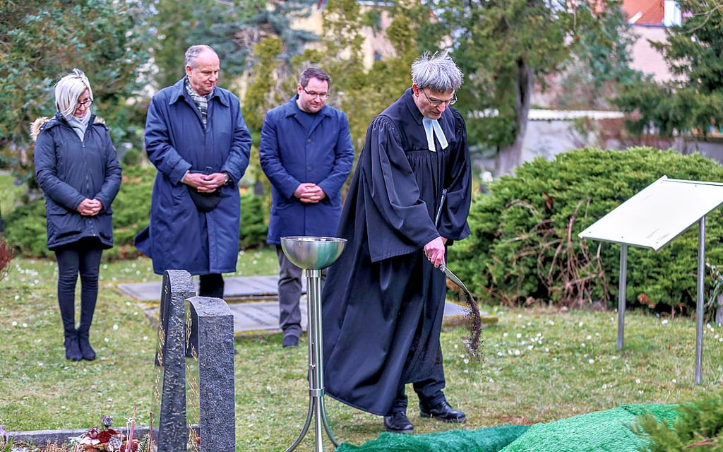 Pfarrer Rüdiger Worbes (r.) streut Erde über die historischen Gebeine, die nun auf dem alten Friedhof ruhen.