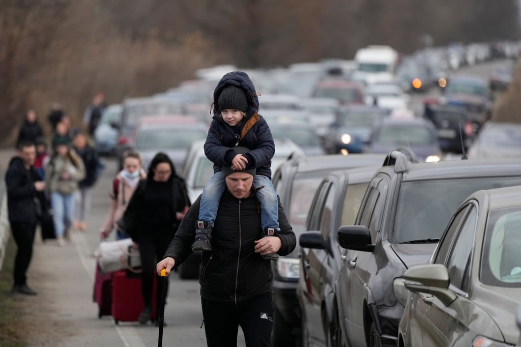 Ukrainische Flüchtlinge gehen mit ihrem Gepäck an Fahrzeugen entlang, die am Grenzübergang stehen.