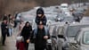 Ukrainische Flüchtlinge gehen mit ihrem Gepäck an Fahrzeugen entlang, die am Grenzübergang stehen.