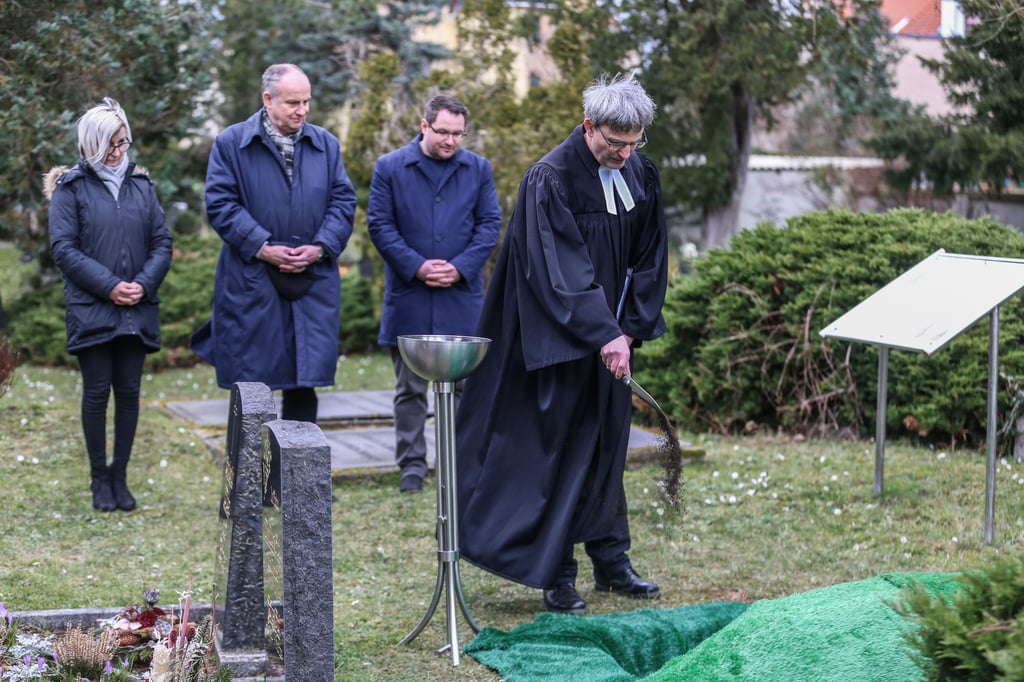 Pfarrer Rüdiger Worbes (r.) streut Erde über die historischen Gebeine, die nun auf dem alten Friedhof ruhen.