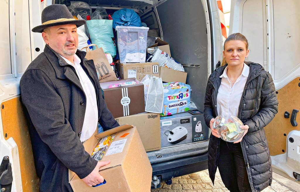 Daniel Wolf-Dziura steht vor dem schon gut gefüllten Transporter und übergibt Malgorzata Gomolka ein Paket mit Lebensmitteln.