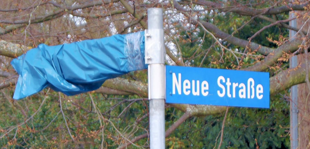 Das Schild „Neue Gartenstraße“ wurde wohl etwas voreilig angebracht. Nun musste es versteckt werden. In anderen umbenannten Straßen sind die alten Schilder noch rot durchgestrichen vorhanden.