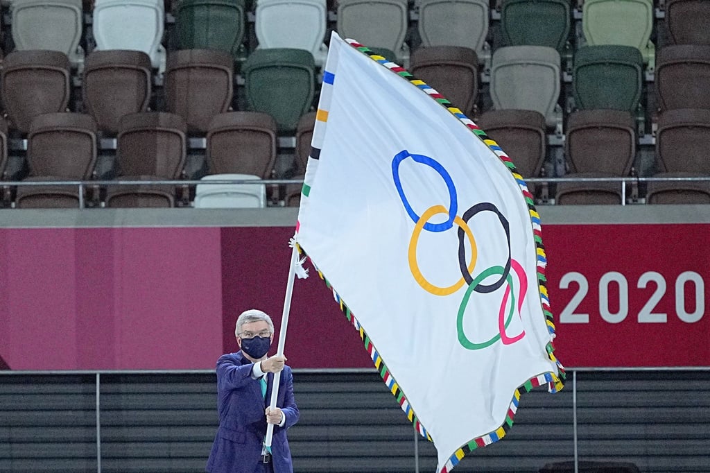 IOC-Präsident Thomas Bach hält die Fahne olympische Fahne hoch.