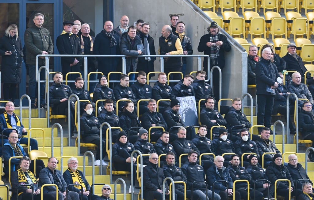 Spieler der SG Dynamo Dresden und Gäste sitzen während der öffentlichen Gedenkfeier zu Ehren von Hans-Jürgen „Dixie“ Dörner im Rudolf-Harbig-Stadion.