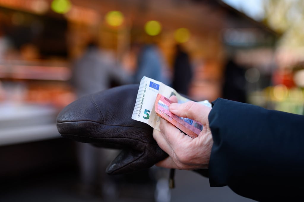 Eine Frau steht an einem Marktstand und hält das Bargeld für ihren Einkauf bereit.