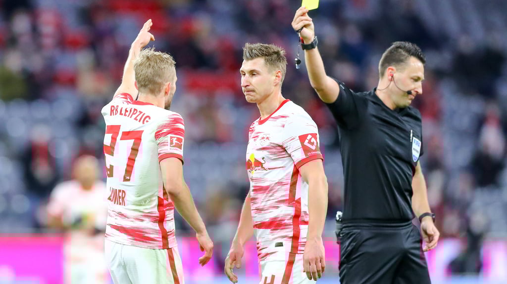 Schiedrichter Sven Jablonski zeigt Konrad Laimer im Spiel gegen den FC Bayern (l.) die gelbe Karte.