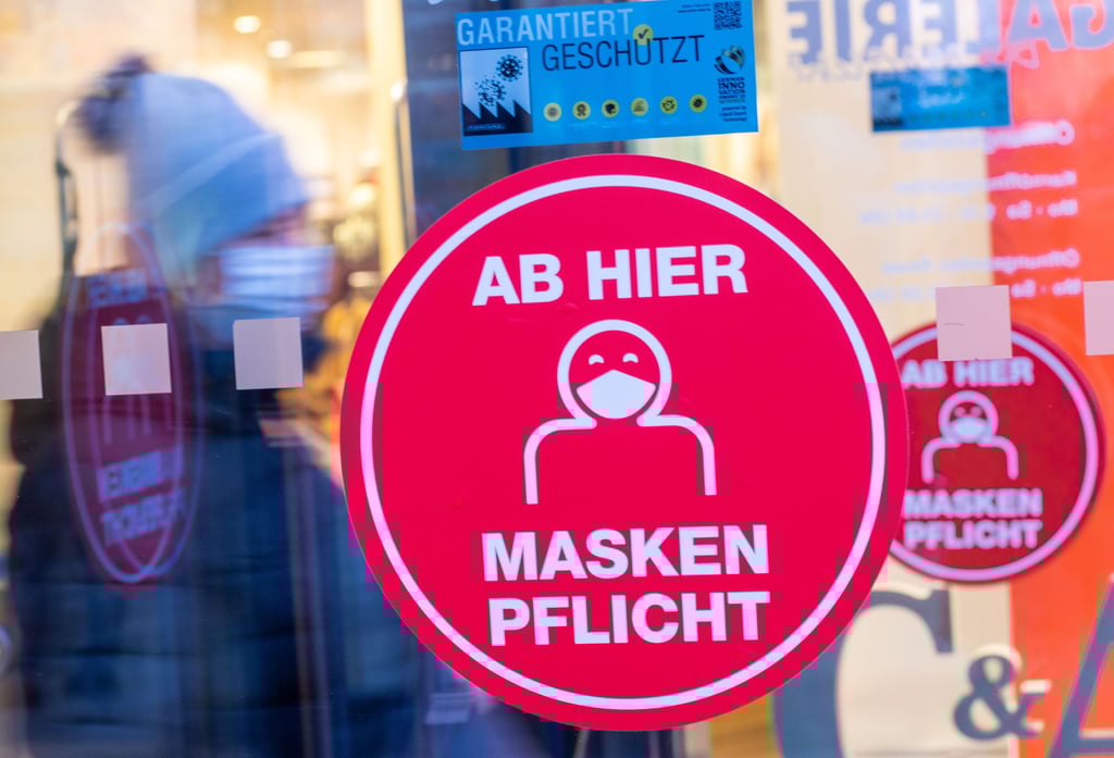 Ein Aufkleber an der Glastür eines Einkaufszentrums weist auf die Maskenpflicht hin. Corona-Schutzmaßnahmen.