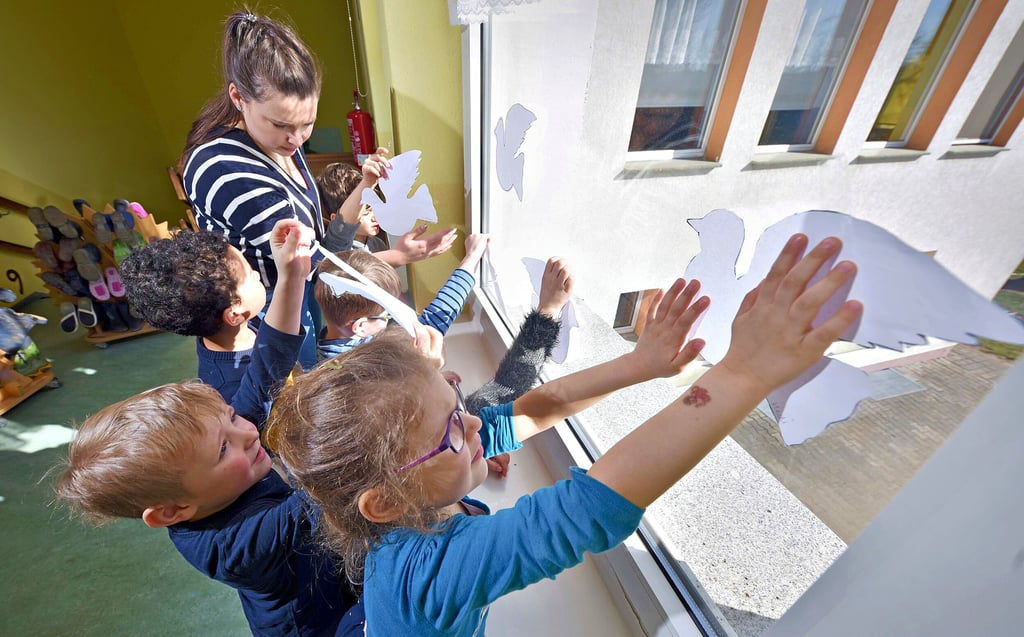 Die Kinder der Mäuschen-Gruppe bringen mit Erzieherin Julia Wirth ihre selbstgebastelten Friedenstauben am Fenster an.