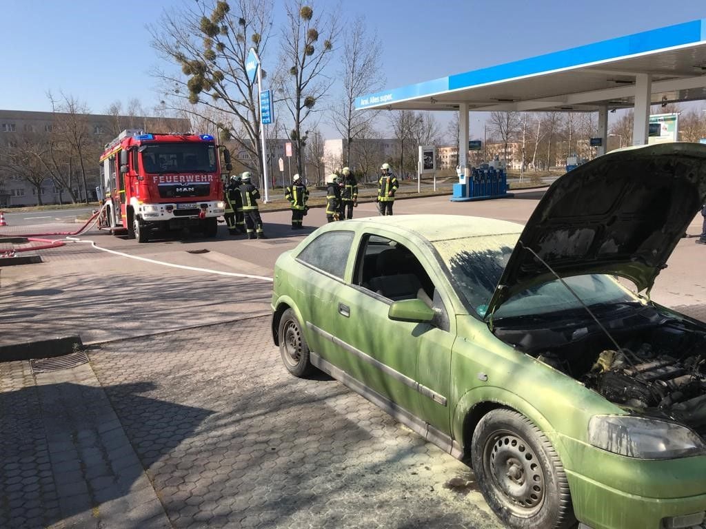 Das ausgebrannte Auto, dahinter die Feuerwehr.