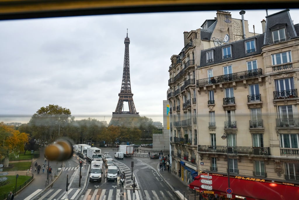 Aus dem Fenster der Pariser Metro ist hinter Wohnhäusern der Eiffelturm zu sehen - samt des üblichen Straßenrkehrs.