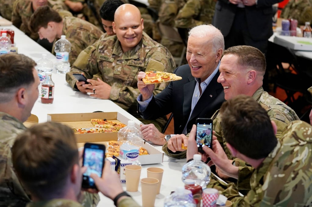 US-Präsident Biden (M) isst während seines Besuchs bei der 82. Luftlandedivision der US-Armee ein Stück Pizza.
