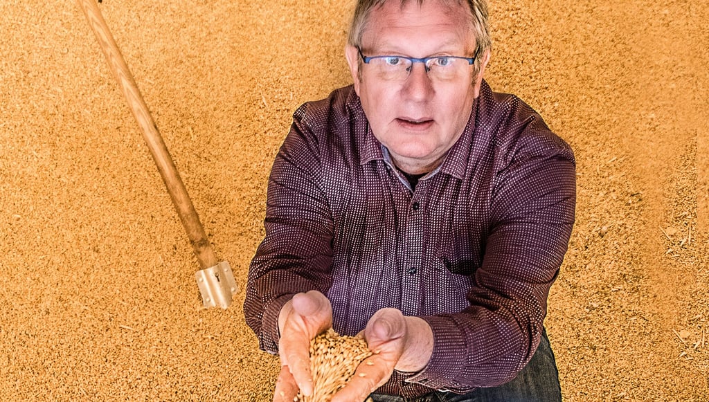 Thomas Külz kniet auf einem Anhänger mit Gerste. Das Getreide ist so gefragt wie lange nicht mehr.