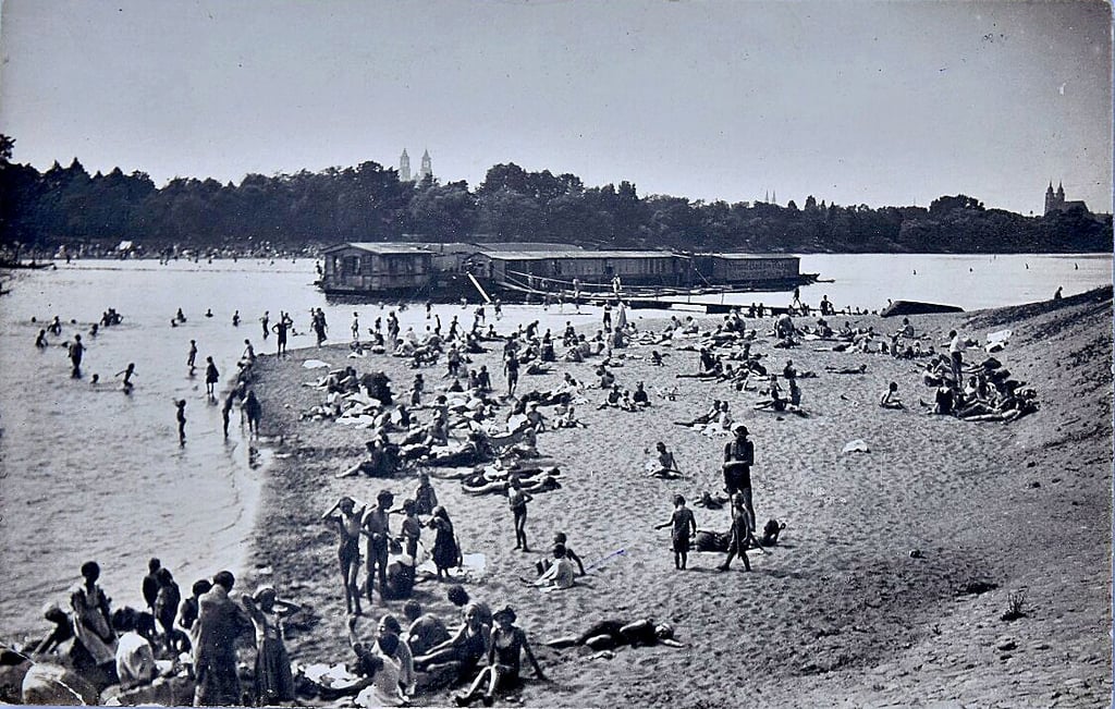 Ein voller Badestrand am Cracauer Wasserfall in Magdeburg. Im Hintergrund dockt eine Badeanstalt in der Alten Elbe.