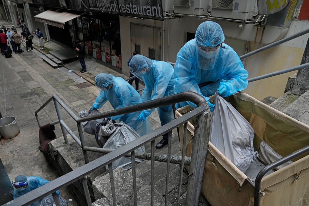 Hotelangestellte in Hongkong tragen Schutzkleidung und entsorgen Müll aus einem Hotel, das zur Isolation genutzt wird.