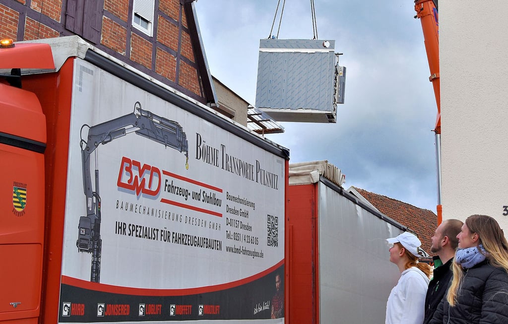 Mitarbeiter der Bäckerei und Passanten verfolgen das Einschweben der etwa viereinhalb Tonnen schweren Fracht. Durch das offene Dach „fliegt“ der neue Ofen direkt in die Backstube.