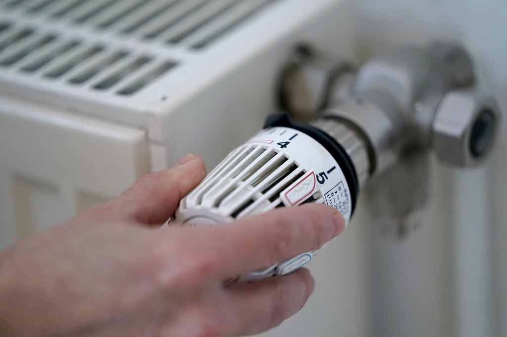 Eine Frau dreht an einem Heizungsthermostat.