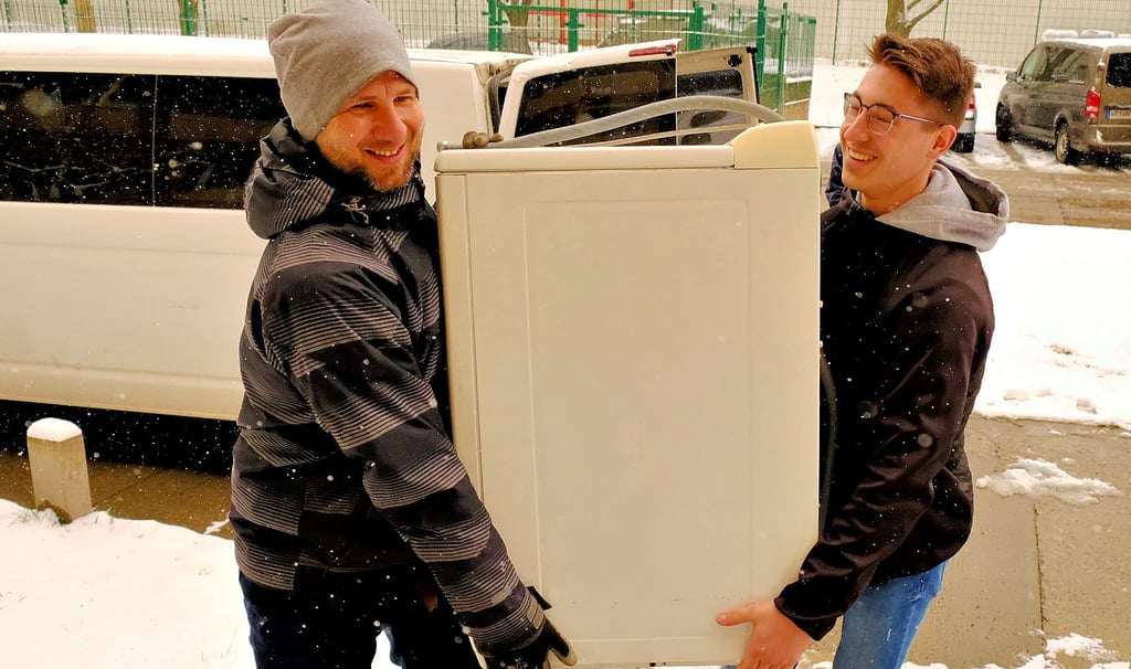 Bennet Dörge und Anton Weiser von der Stadtverwaltung Blankenburg tragen eine gespendete Waschmaschine in eine der einzurichtenden Wohnungen im Regenstein.