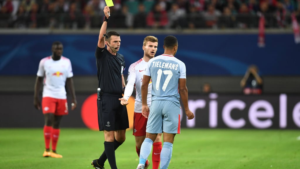 Michael Oliver zeigt Youri Tielemans im Spiel zwischen RB Leipzig und der AS Monaco die gelbe Karte, Timo Werner schaut dabei zu.