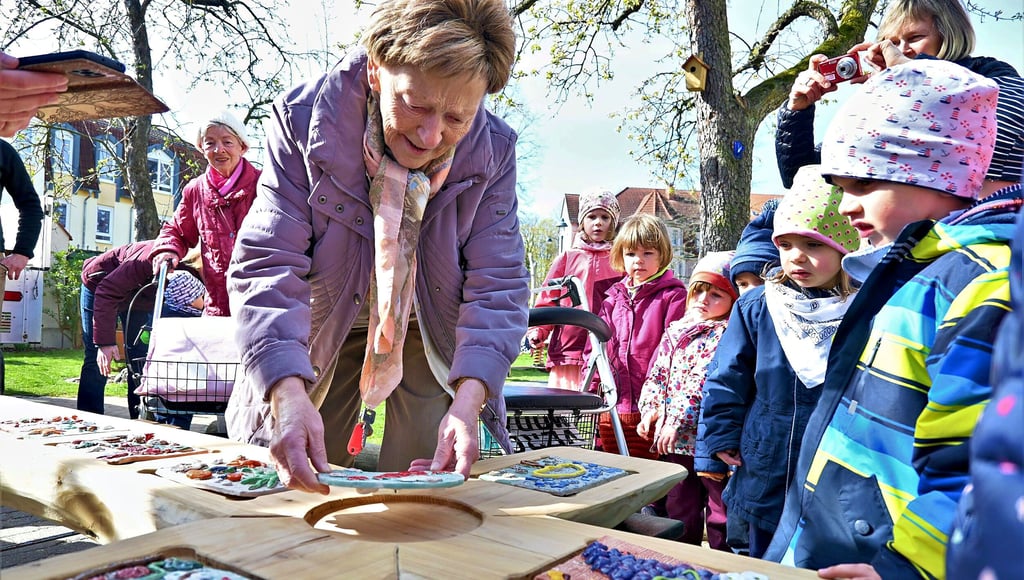 Brigitte Körner ist Bewohnerin der Seniorenresidenz in Torgau und befestigt hier eine der Keramiktafeln, die in Zusammenarbeit mit den Kindergruppen der Kita Piusstift entstanden sind, am Kreuz für das Kirchenwäldchen.