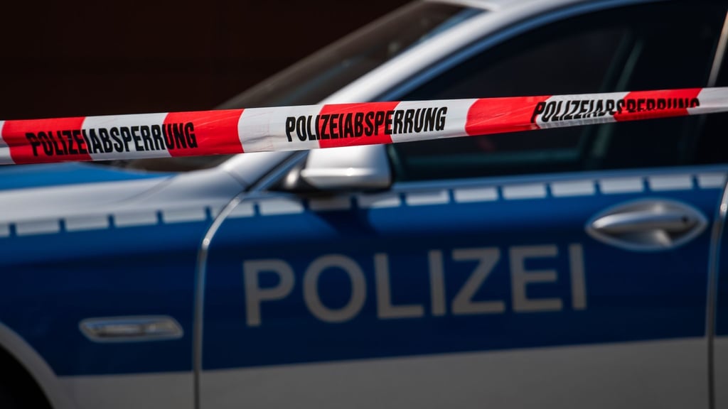 Ein Polizeiauto steht hinter einem Absperrband der Polizei.