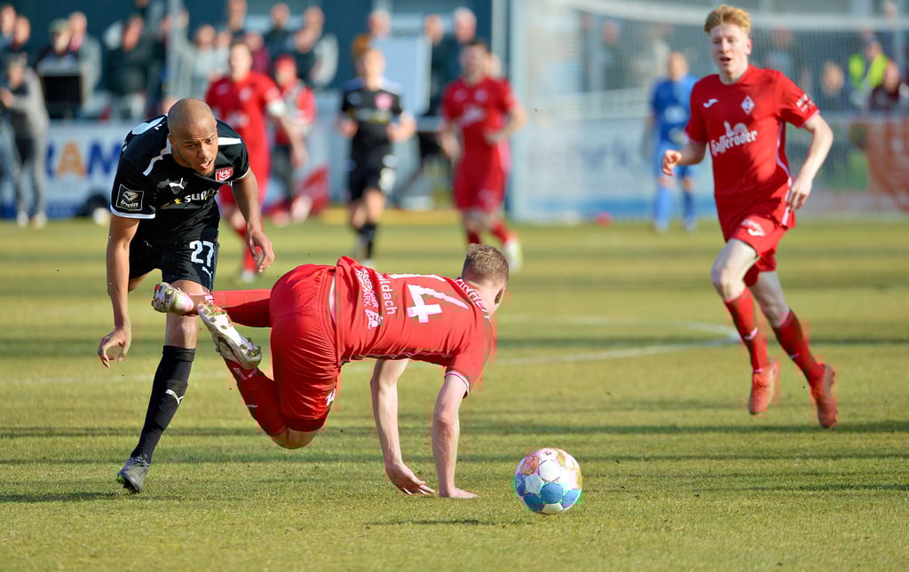 Kevin Hildach, der zentrale Mittelfeldspieler von Einheit Wernigerode (14) – Torschütze zum 1:1 – beim Pokalsieg gegen den Halleschen FC am 26. März 2022 im Halbfinale des Sachsen-Anhalt-Pokals im Zweikampf mit Louis Samson (27). Rechts der Siegtorschütze zum 2:1, Erik Weinhauer, zentrales Mittelfeld.Thomas Wartmann