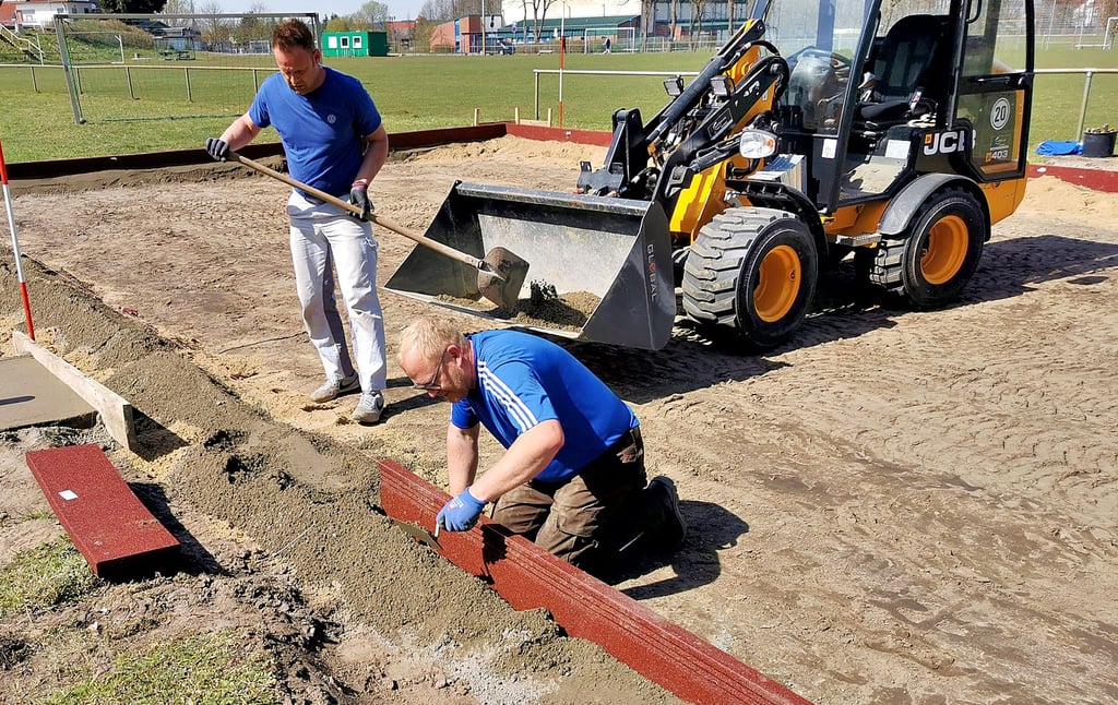 Olaf Reek (rechts) und Andreas Brun setzten weinrote Gummiborde als Umrandung für den neuen Beachvolleyballplatz am Klötzer Stadion. Die Einweihung erfolgt am 1. Mai.