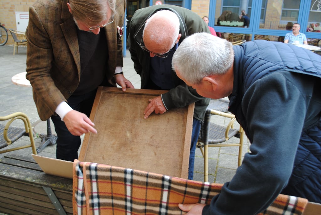 Hartwig Bretschneider, Dieter Fettback und Maurice Philip Remy untersuchen in Stendal die Rückwand des Ölgemäldes.