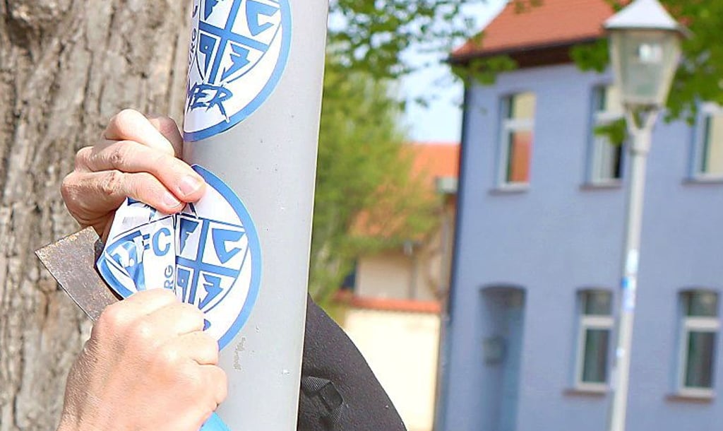 Mit einem Spatel wird ein FCM-Aufkleber von einem Mast entfernt.