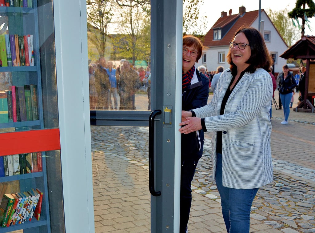 Britt Godisch (rechts) und Kerstin Mosonyi schließen die Tür zur Bücherzelle in dem Halberstädter Ortsteil Emersleben auf.