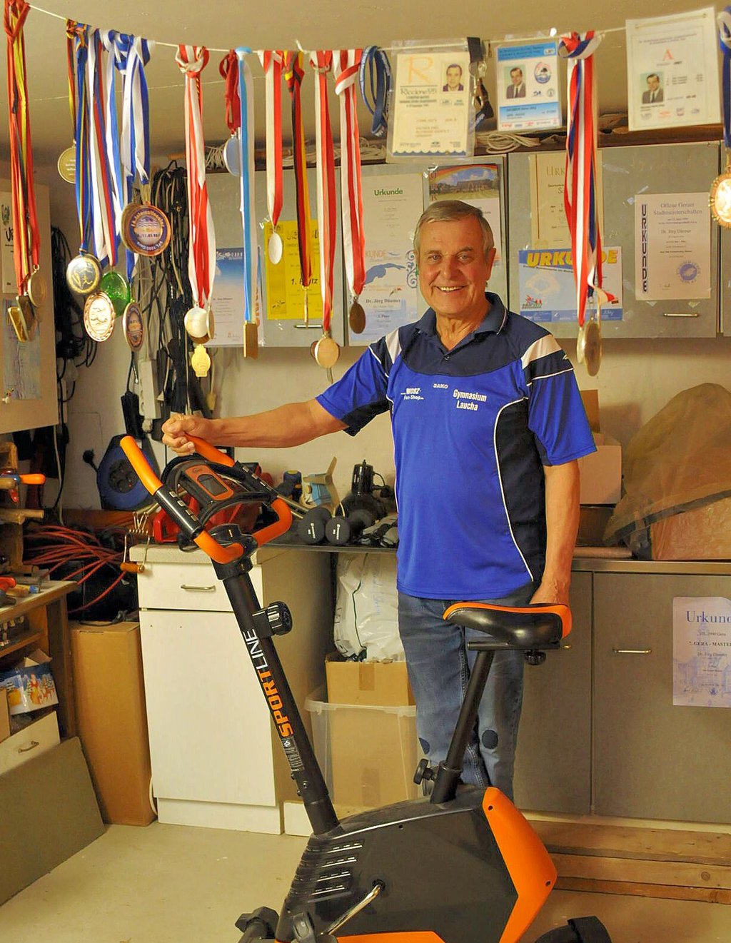 Leute von nebenan: Jörg Däumer (Bad Bibra). Auf dem Ergometer im Keller seines Hauses trainiert der heute 71-Jährige im Winter seine Fitness - "umrahmt" von Medaillen und Wettkampf-Akkreditierungen.