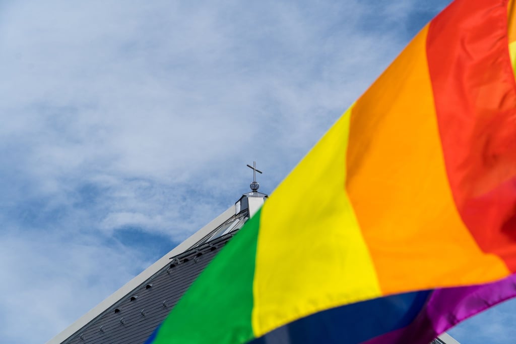 Eine Regenbogenfahne weht vor einer Kirche.
