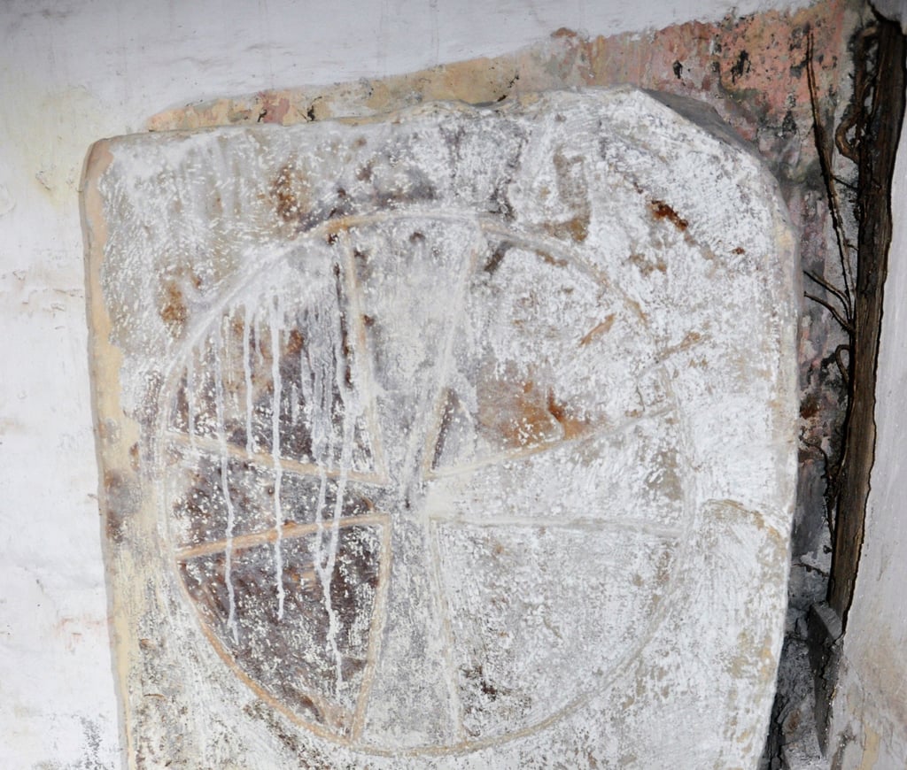 Der Kreuzstein steht schon ewig neben der Eingangstür ins Kircheninnere. Allerdings war er weiß bemalt und verschmolz fast mit der Wand, an der er lehnte. Erste, leichte Renigungsarbeiten zur Beprobung brachten nun rote Farbe ans Licht.