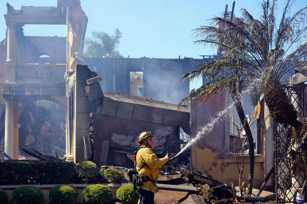 Der Feuerwehrmann Mike Mejia vom National City Fire Dept. löscht noch brennende Stellen an einem Haus nach dem Küstenfeuer in Laguna Niguel.