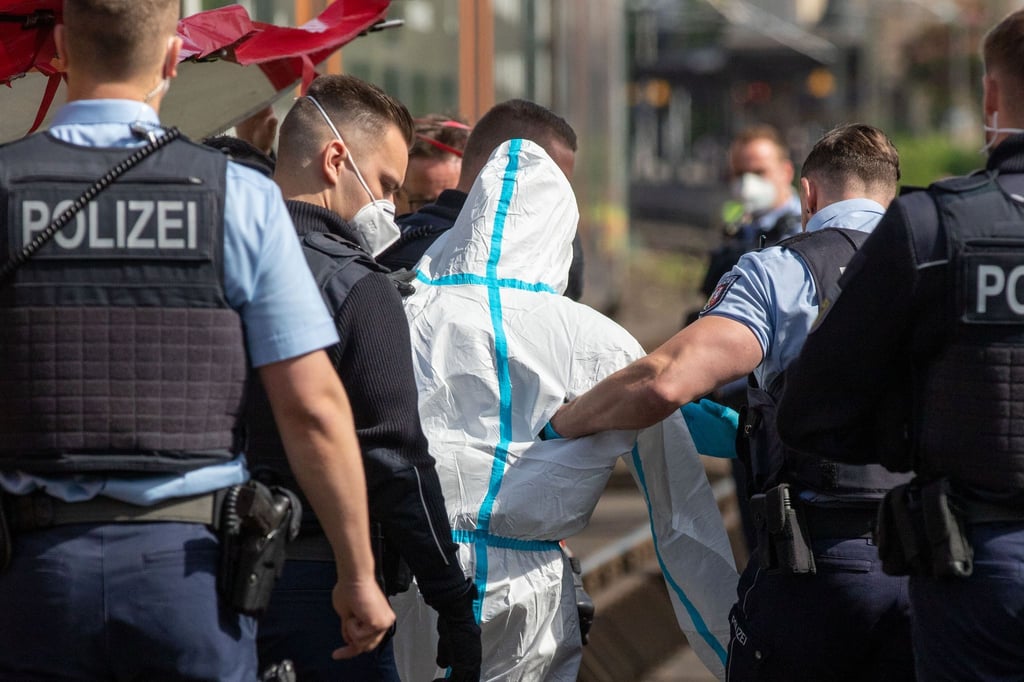 Polizisten führen den mutmaßlichen Täter ab. Der Mann soll in einer Regionalbahn mit einem Messer auf Reisende eingestochen haben.